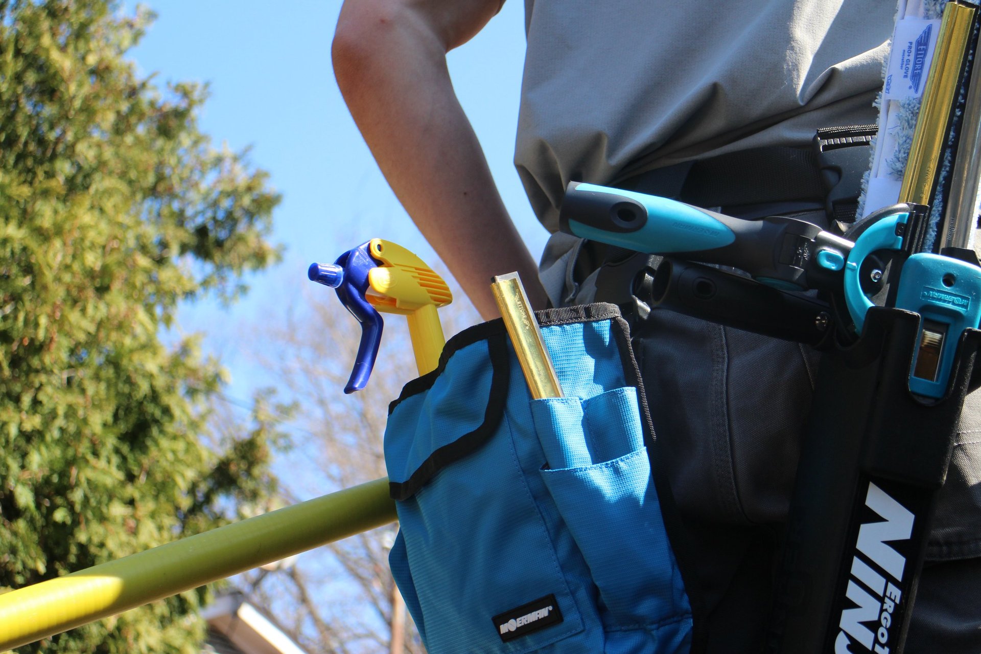 Worker in blue work gloves and tool belt handling a yellow pole with blue attachment outdoors