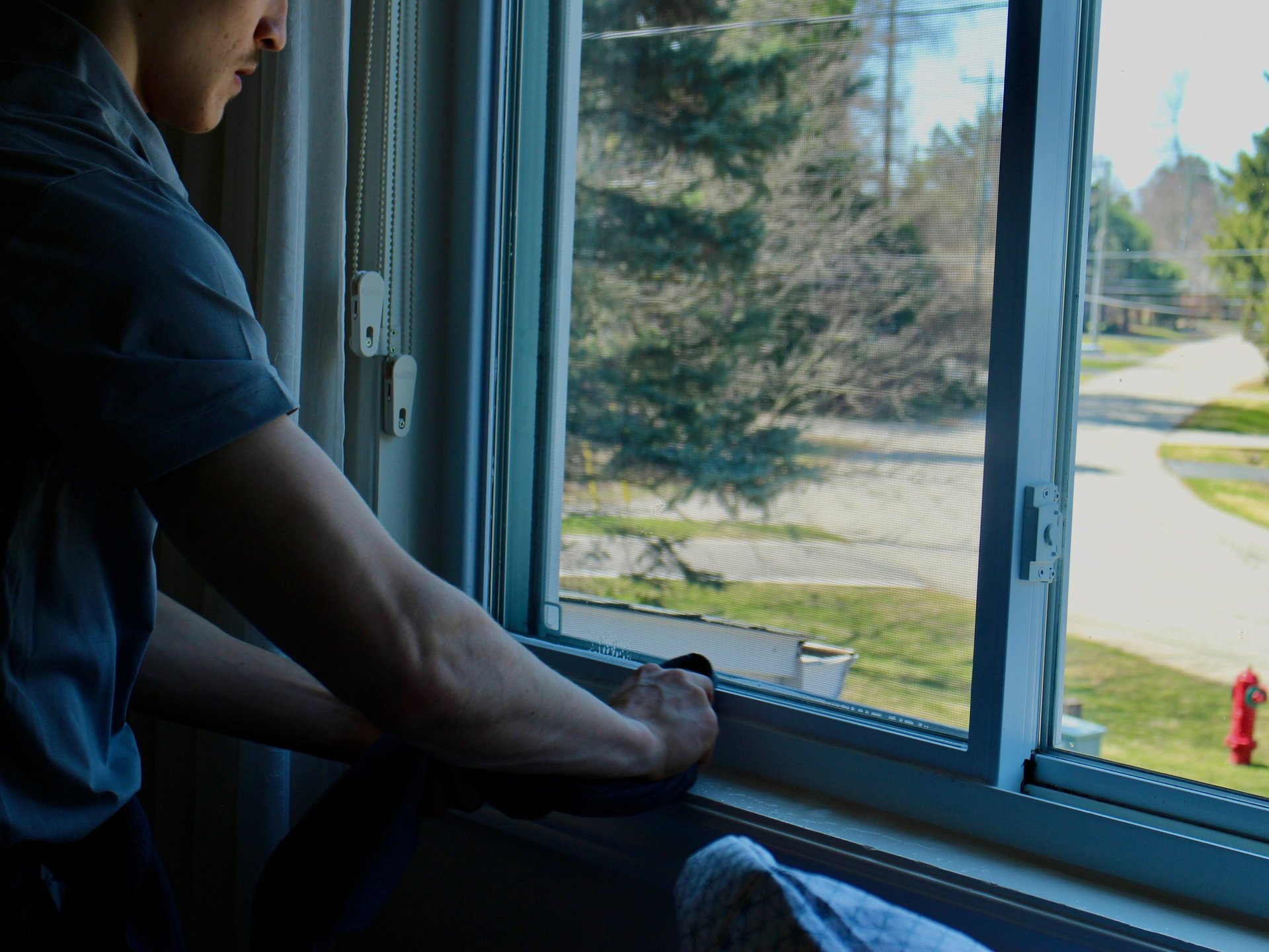 Person in dark blue shirt looking out a large window at a residential street and trees