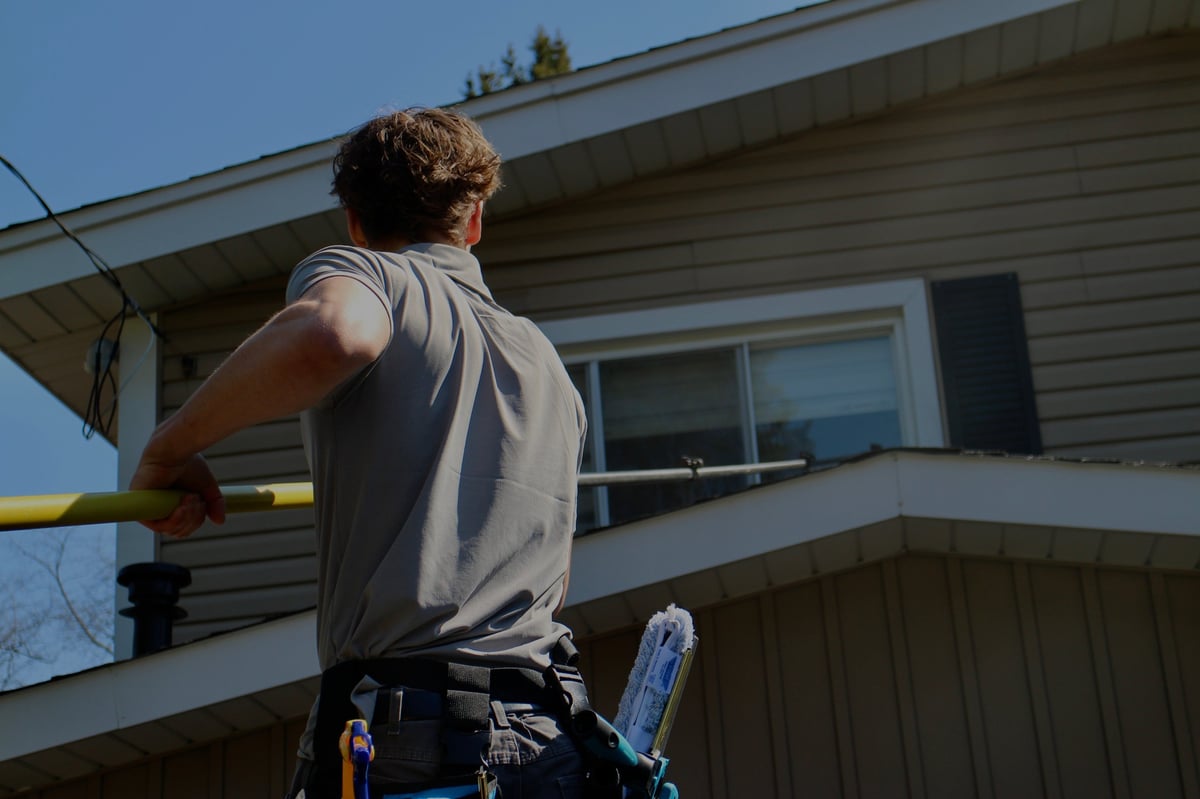 Worker standing on ladder with tool belt working on exterior of residential house
