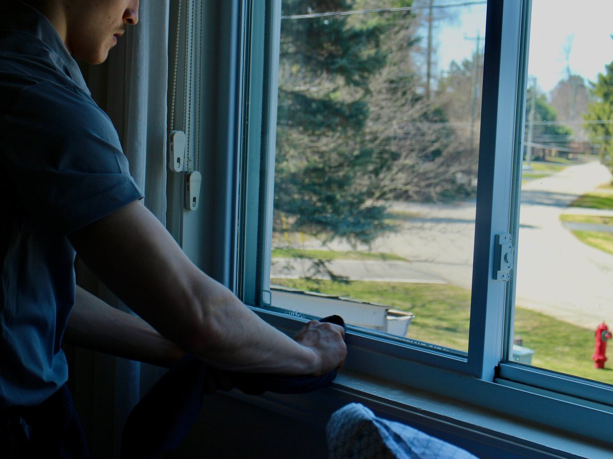 Person in blue shirt looking out window at suburban street and trees