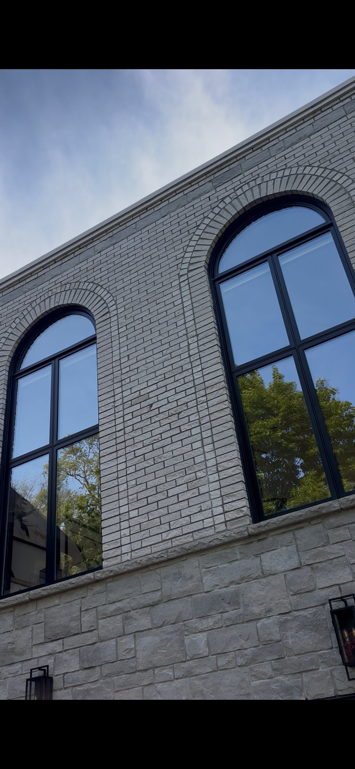 Two large arched windows with black frames on a light gray brick building facade